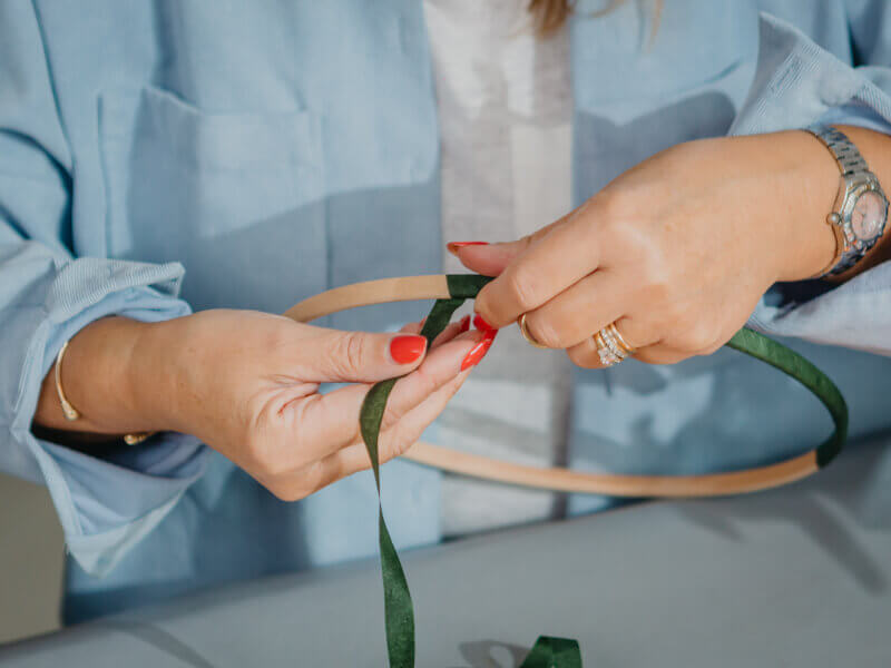 A person wrapping a wooden circle in green ribbon to prep their flower wreath.